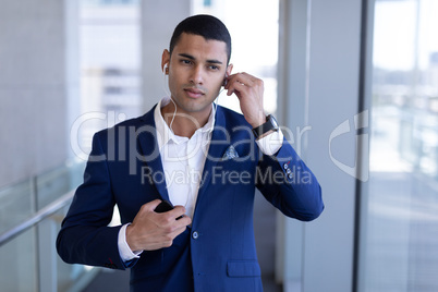 Young mixed-race businessman listening music on mobile phone in modern office