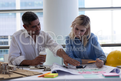Caucasian architects discussing over blueprint at desk in office