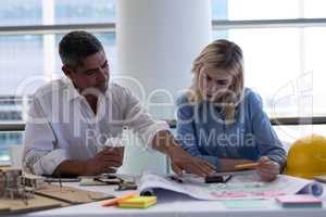 Caucasian architects discussing over blueprint at desk in office