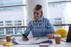 Blonde Caucasian female architect using mobile phone at desk in office