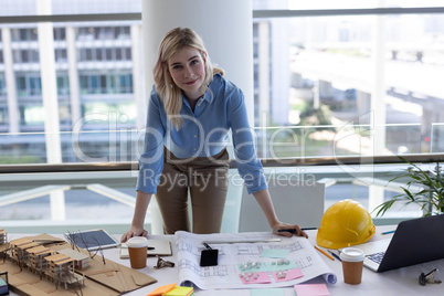 Blonde Caucasian female architect looking at camera at desk in office