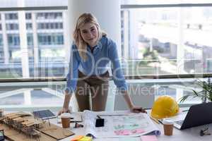 Blonde Caucasian female architect looking at camera at desk in office