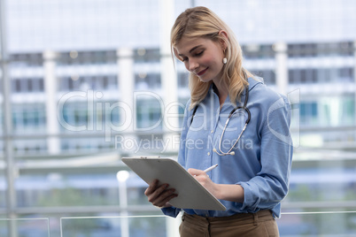 Blonde Caucasian female doctor writing on clipboard in clinic