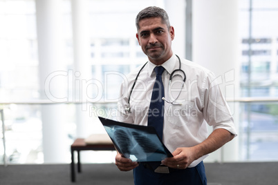 Caucasian male doctor with x-ray looking at camera in clinic