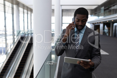 African-American businessman using digital tablet while talking on mobile phone in office