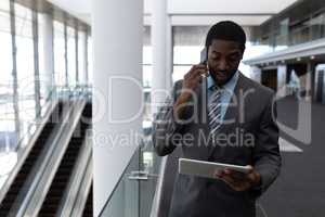 African-American businessman using digital tablet while talking on mobile phone in office