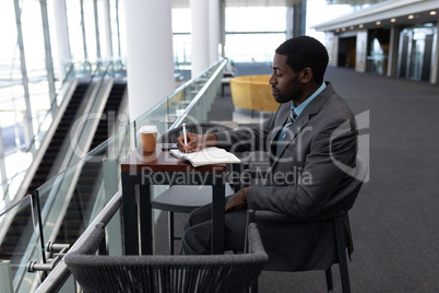 African-American businessman sitting at table and writing on diary in office