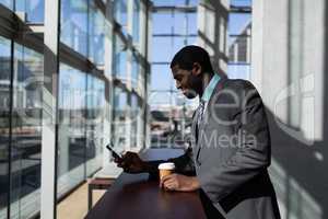 African-American businessman with coffee cup using mobile phone in office