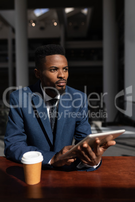 African-American businessman with digital tablet looking away at table in office