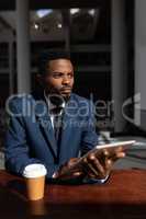 African-American businessman with digital tablet looking away at table in office