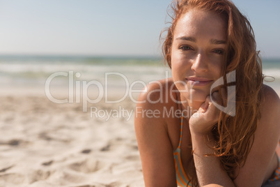 Young Caucasian woman in bikini lying on the sand and looking at camera on the beach