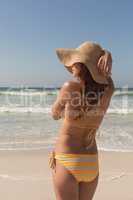 Young Caucasian woman in bikini and hat standing on the beach