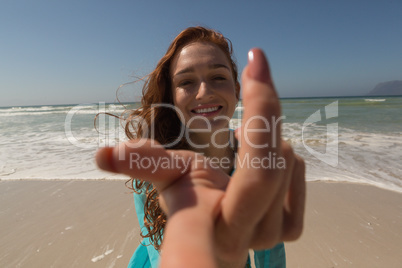 Young Caucasian woman hand reaching towards the camera at beach
