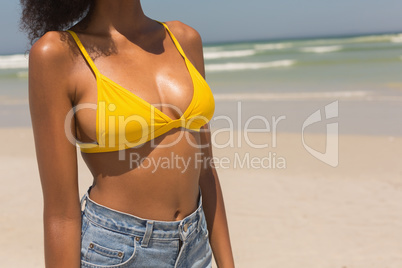 Mid section of young African American woman in yellow bikini standing on beach