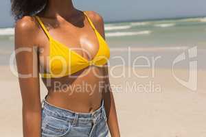 Mid section of young African American woman in yellow bikini standing on beach
