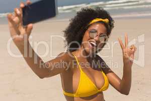 Young African American woman in yellow bikini and sunglasses taking selfie
