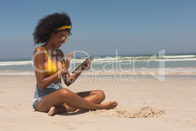 Young African American woman in yellow bikini and sunglasses using digital tablet