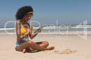Young African American woman in yellow bikini and sunglasses using digital tablet