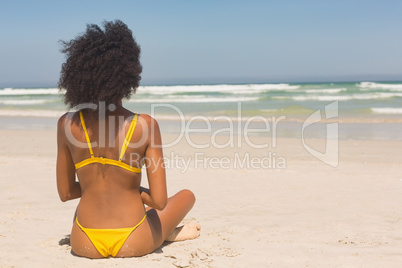 Young African American woman in yellow bikini sitting on the beach