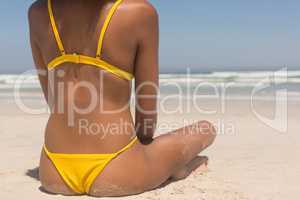 Young African American woman in yellow bikini sitting on the beach