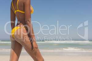 Young African American woman in yellow bikini standing on the beach
