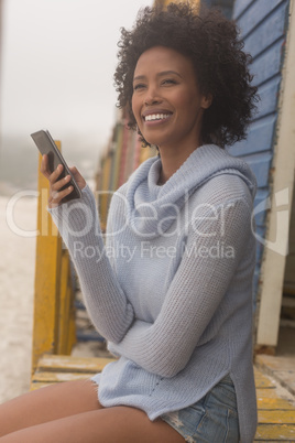 Young African American woman using mobile phone sitting at beach hut