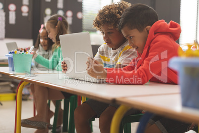 Side view of two mixed-race school boys looking at their laptop in classroom at school