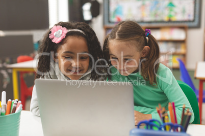 Surface level view of two schoolgirl smiling while they working on their computer