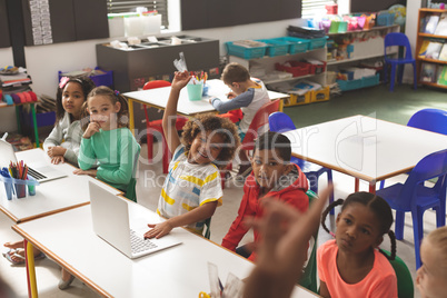 Front view of row of school kids listening their teacher and one of them raising his finger to answe