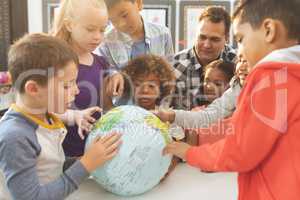 Schoolteacher discusing over a earth globe in classroom at school