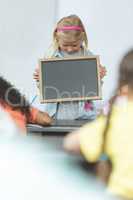 Caucasian schoolgirl holding a slate in classroom at school with his classmates sitting in front of