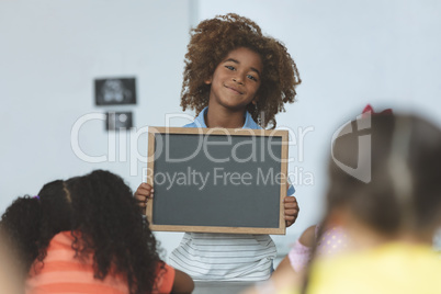 African ethnicity schoolboy holding a slate and looking at camera in classroom