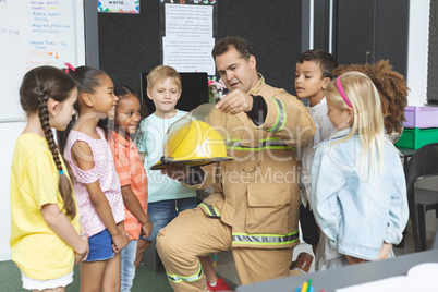Firefighter teaching student about fire safety while holding fire helmet
