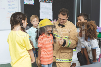 Firefighter interacting with school kids while one of them holding fire helmet on her head