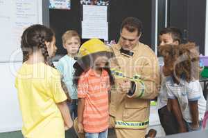 Firefighter interacting with school kids while one of them holding fire helmet on her head
