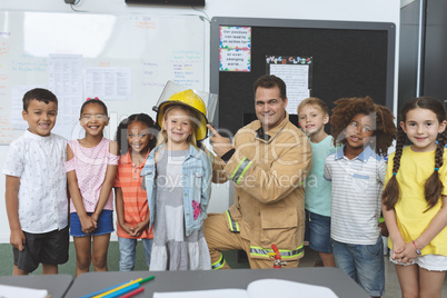 Happy students standing with firefighter in classroom