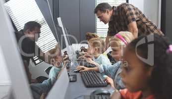 Schoolteacher teaching to school kids how to use computer