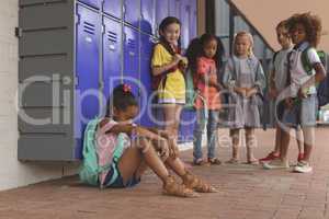 Schoolgirl sitting alone in school corridor while others school kids looking at her