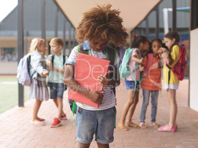 African ethnicity schoolboy holding a red book in arms at school