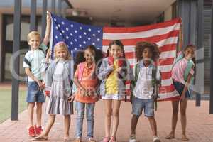 Happy school students standing in corridor while holding american flag