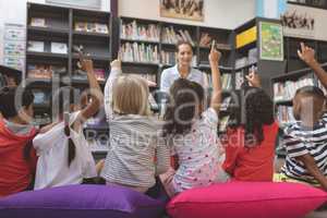 Rear view of school kids raising hand in library to answer at a question