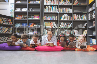 Schoolteacher lying with his school kids and using digital tablet in a library