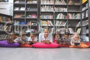 Schoolteacher lying with his school kids and using digital tablet in a library