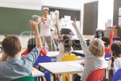School kids raising hands while teacher explaining the functioning of human skeleton in classroom