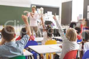 School kids raising hands while teacher explaining the functioning of human skeleton in classroom