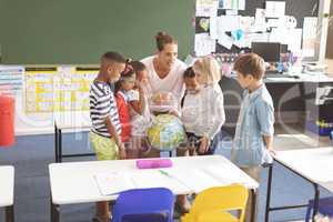 Schoolteacher discussing over the earth globe in classroom