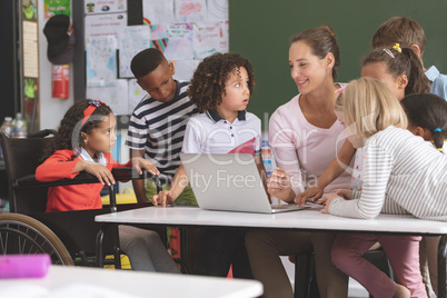 Teacher and students discussing over laptop in classroom