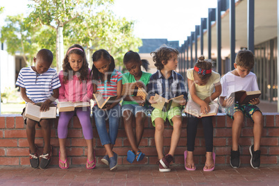 Students reading book while sitting on brick wall at corridor