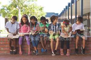 Students reading book while sitting on brick wall at corridor