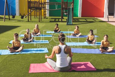 Trainer teaching yoga to students in school playground